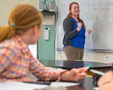 Female teacher standing in front of a classroom writing on a dry erase board