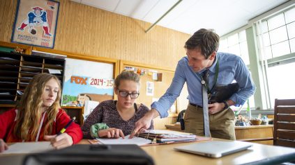 Male teacher helping to teenage female students in a classroom