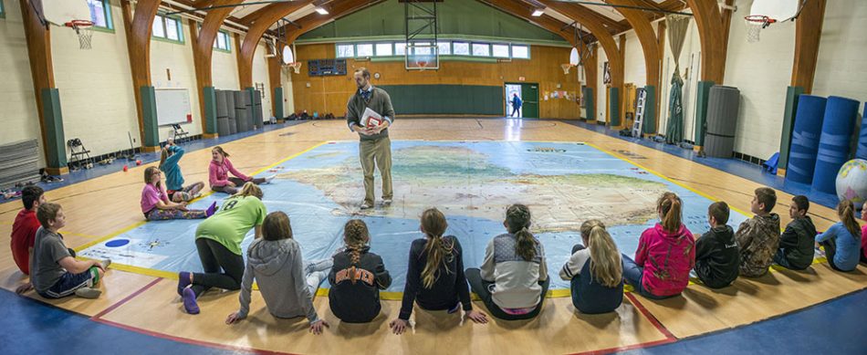 teacher in gym with students and large map on floor