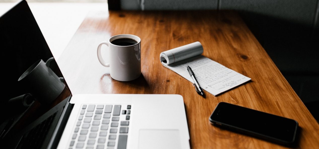 laptop, notepad and pen, mobile phone and mug of coffee