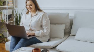 Smiling plus size businesswoman sitting in the living room and working on her laptop computer.