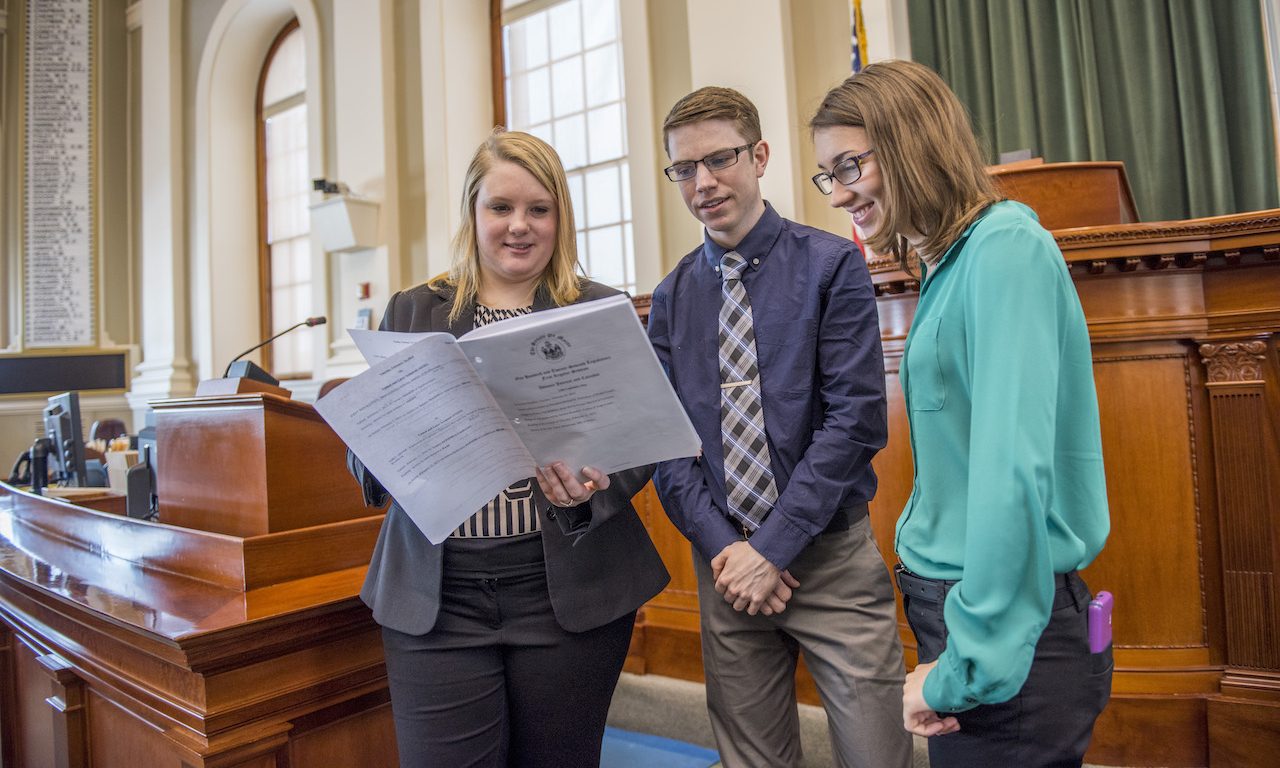 Two students talking with a Maine State Representative in the Maine Capital building