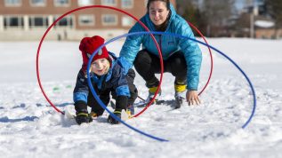 Teacher encouraging preschool student playing in the snow.