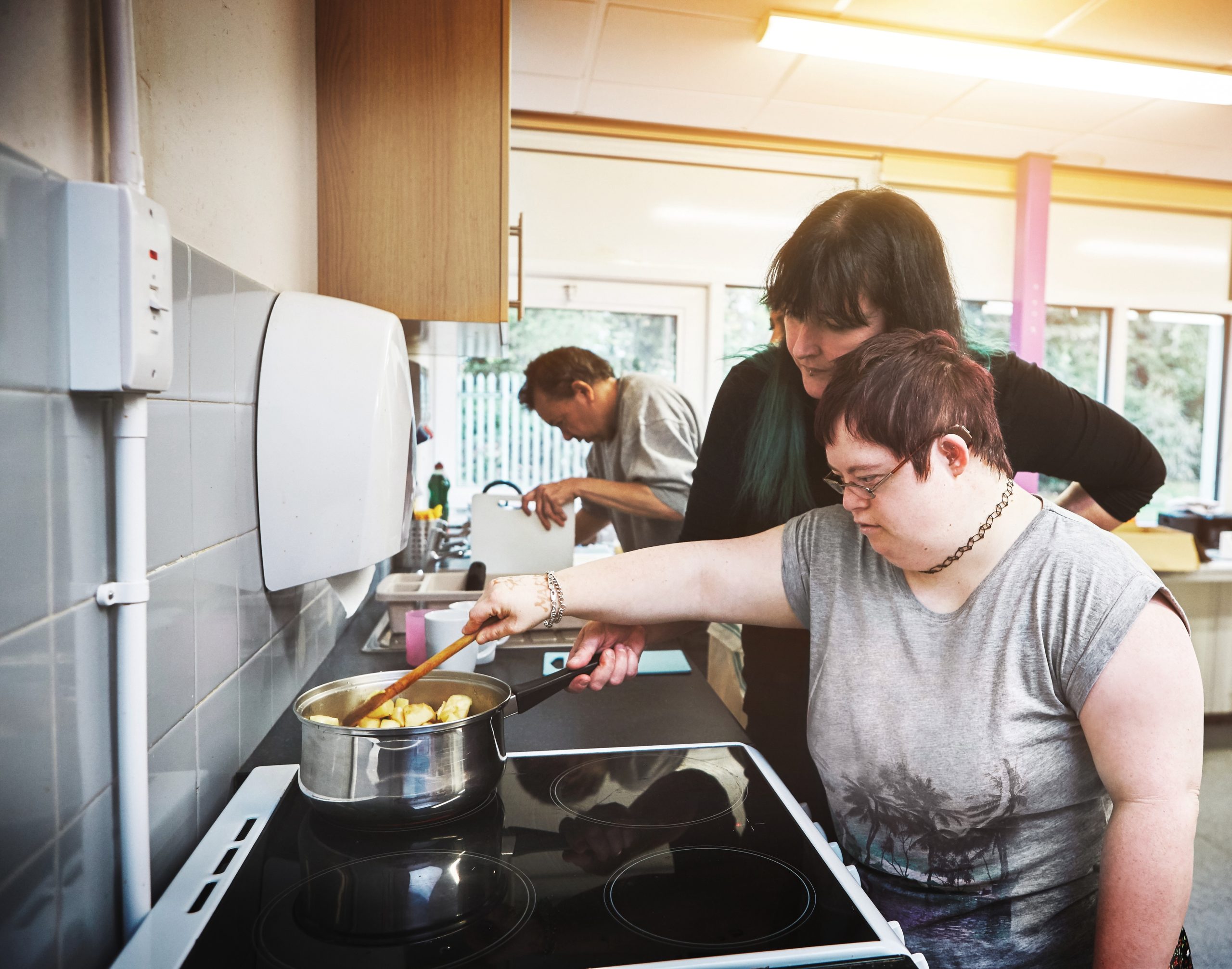 Person helping young adult with disabilities cook