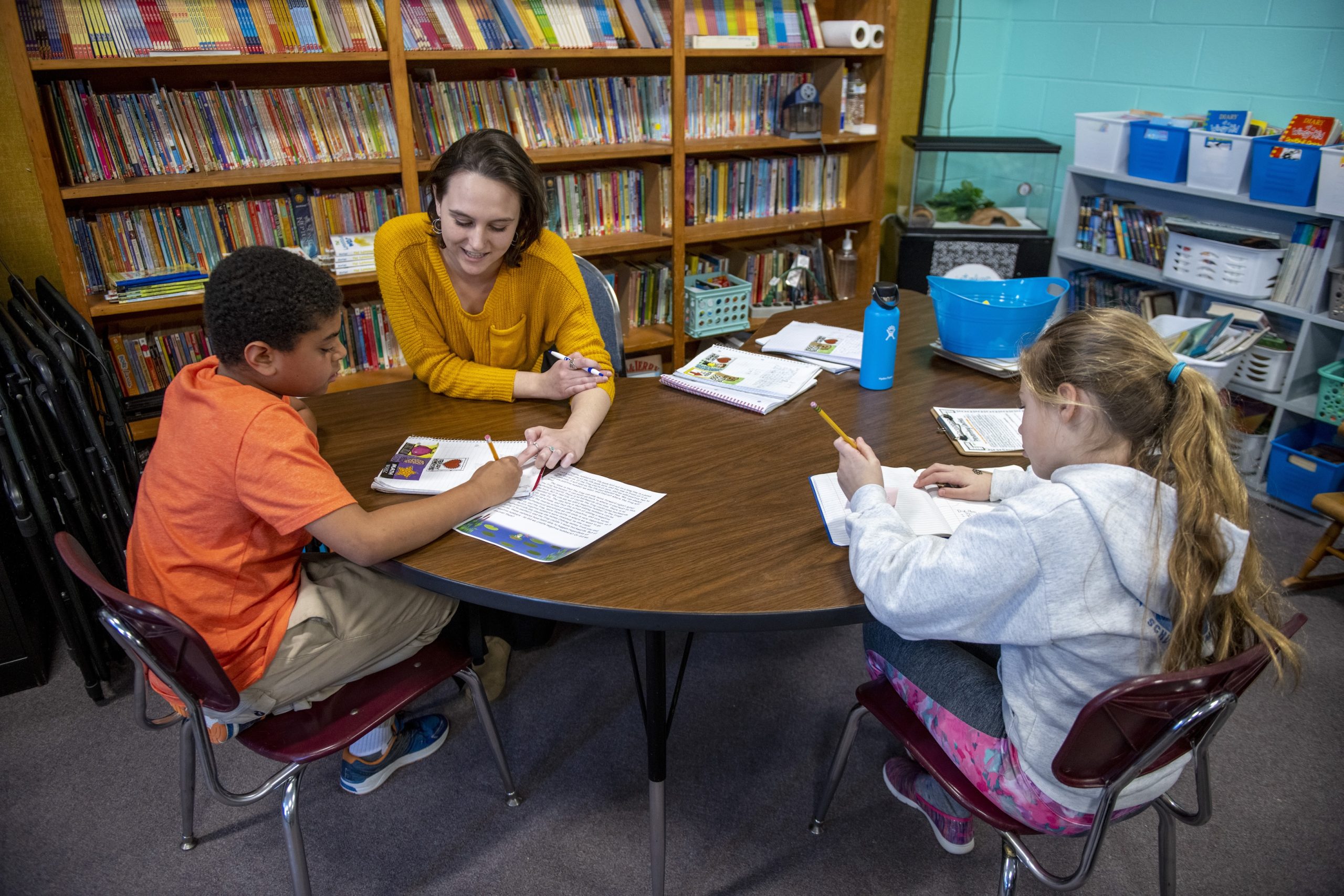 Teacher working with two young students in a library