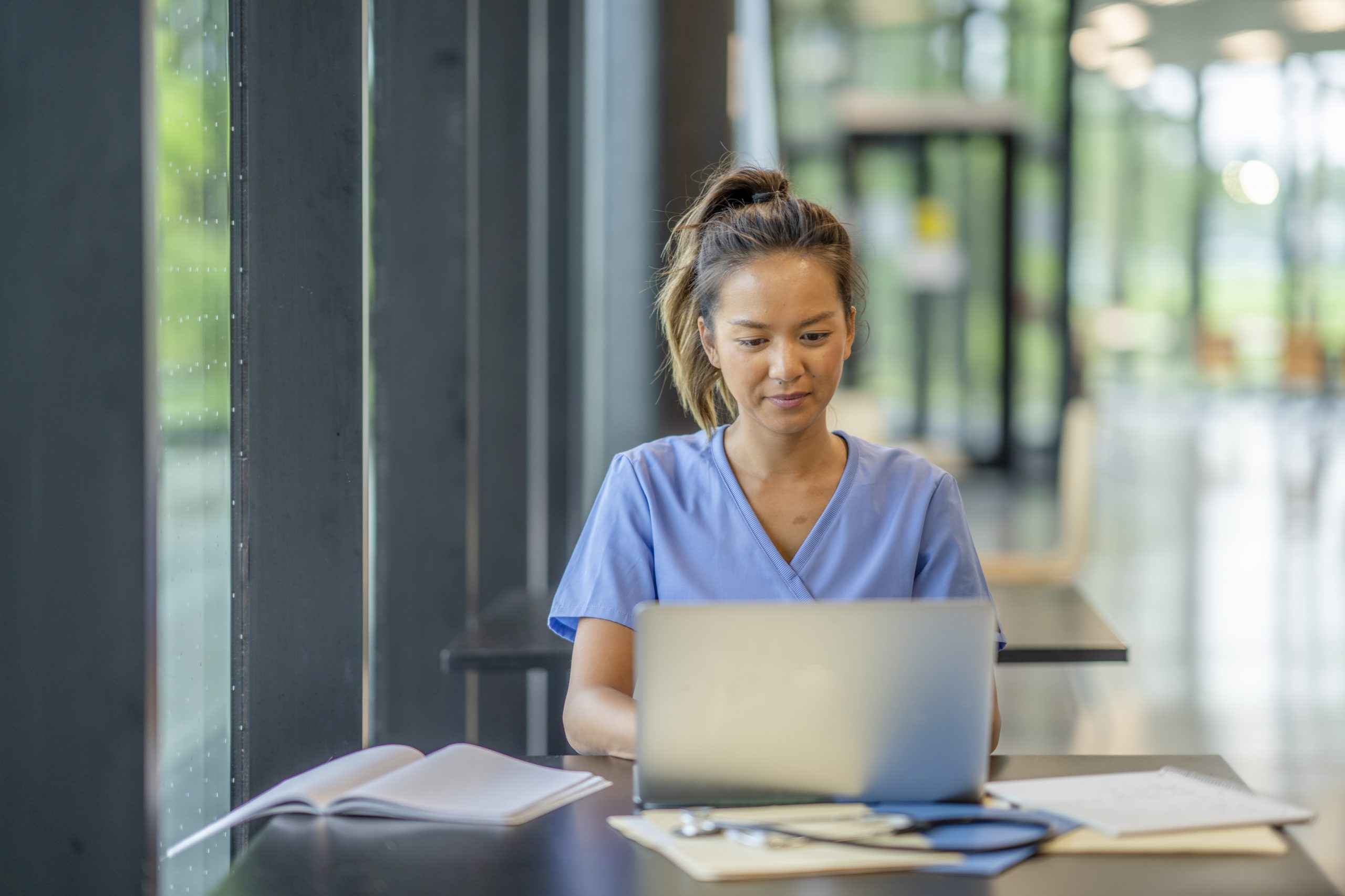 A student in scrubs working on a laptop.