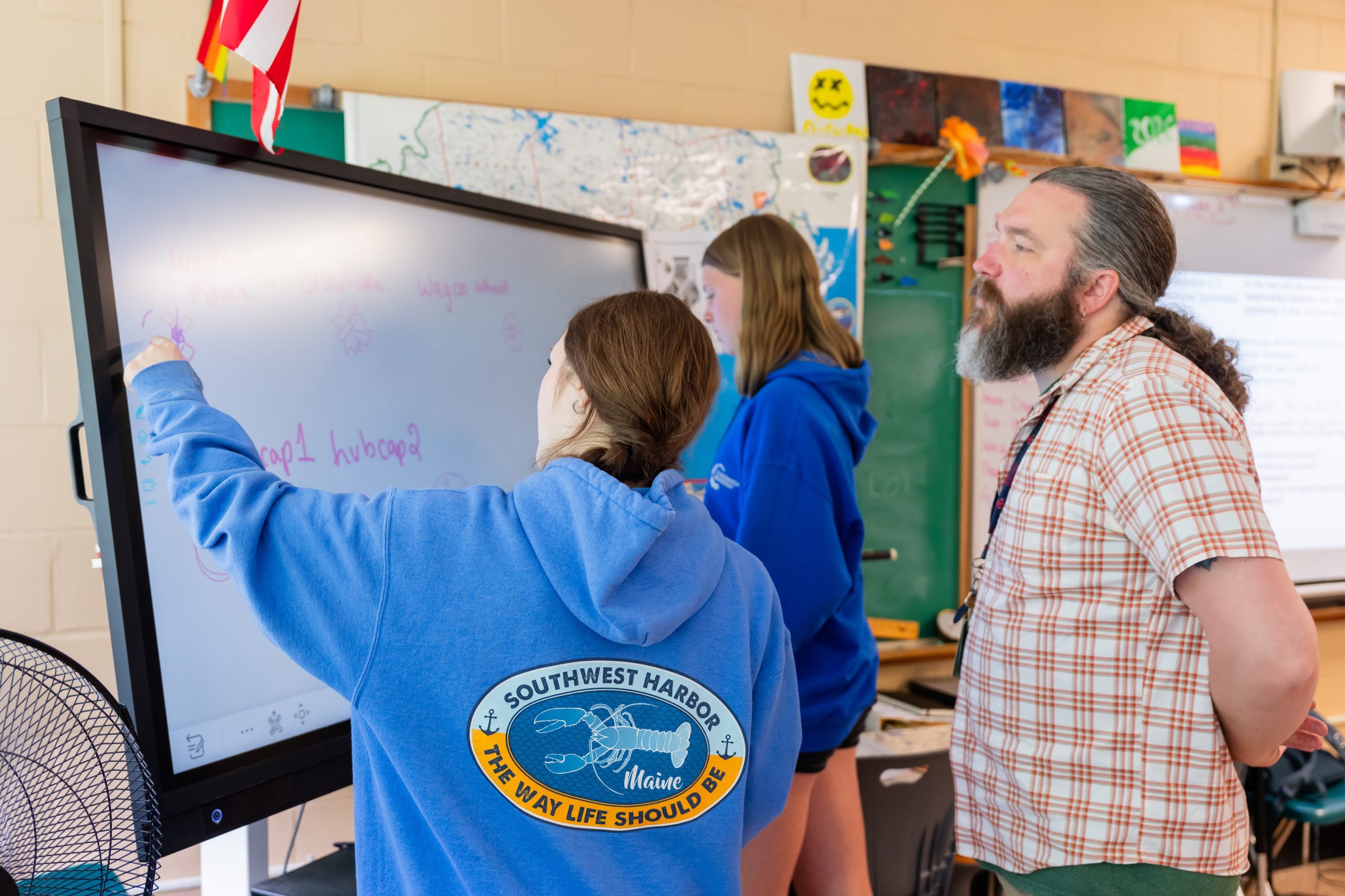 Teacher overseeing two students writing on a whiteboard
